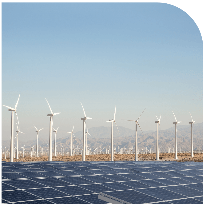 Wind turbines and solar panels in a desert landscape with mountains in the background under a clear blue sky.